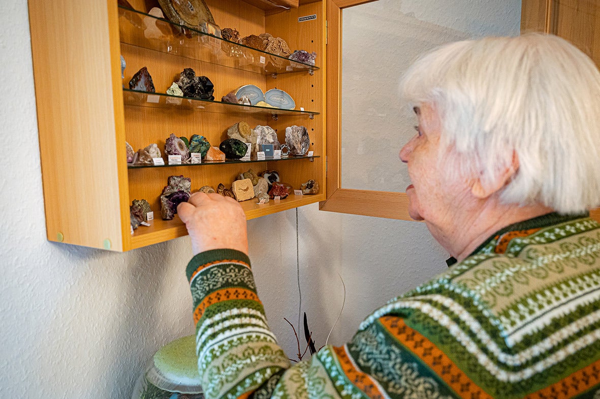 Eine Seniorin steht vor einem Wandschrank und schaut sich verschiedene Steine an.