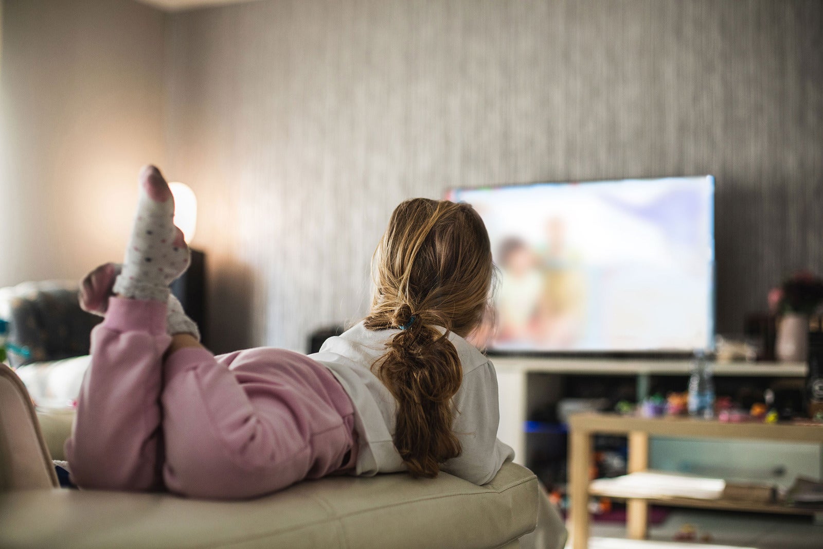Person liegt auf Sofa und schaut TV in gemütlichem Wohnzimmer.