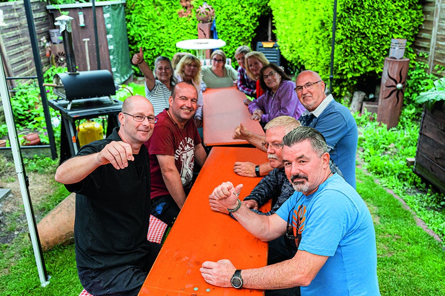 Menschen sitzen gemeinsam an einem Tisch im Garten.