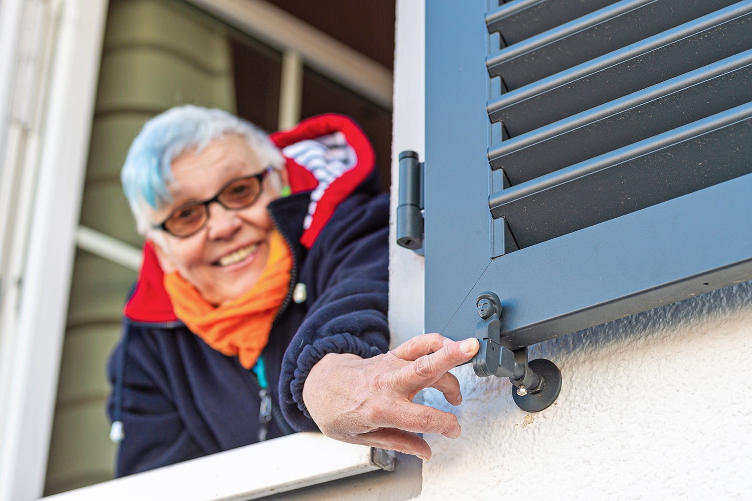 Person streckt Hand aus einem Fenster, greift nach Fensterladen.