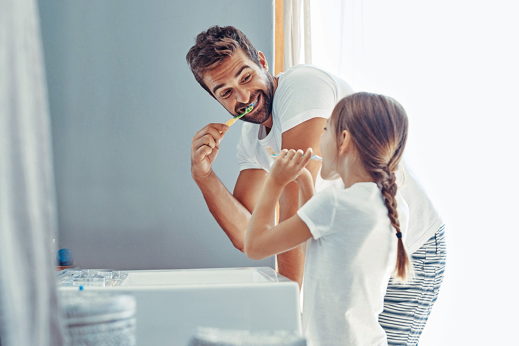 Mann und Kind putzen sich die Zähne im Badezimmer.