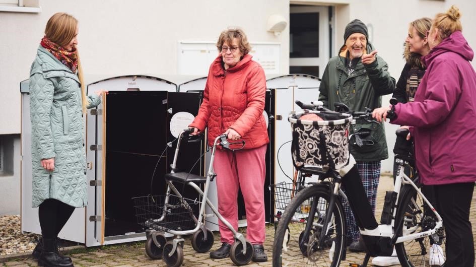 Frau schließt Schuppen, vier Personen unterhalten sich draußen.