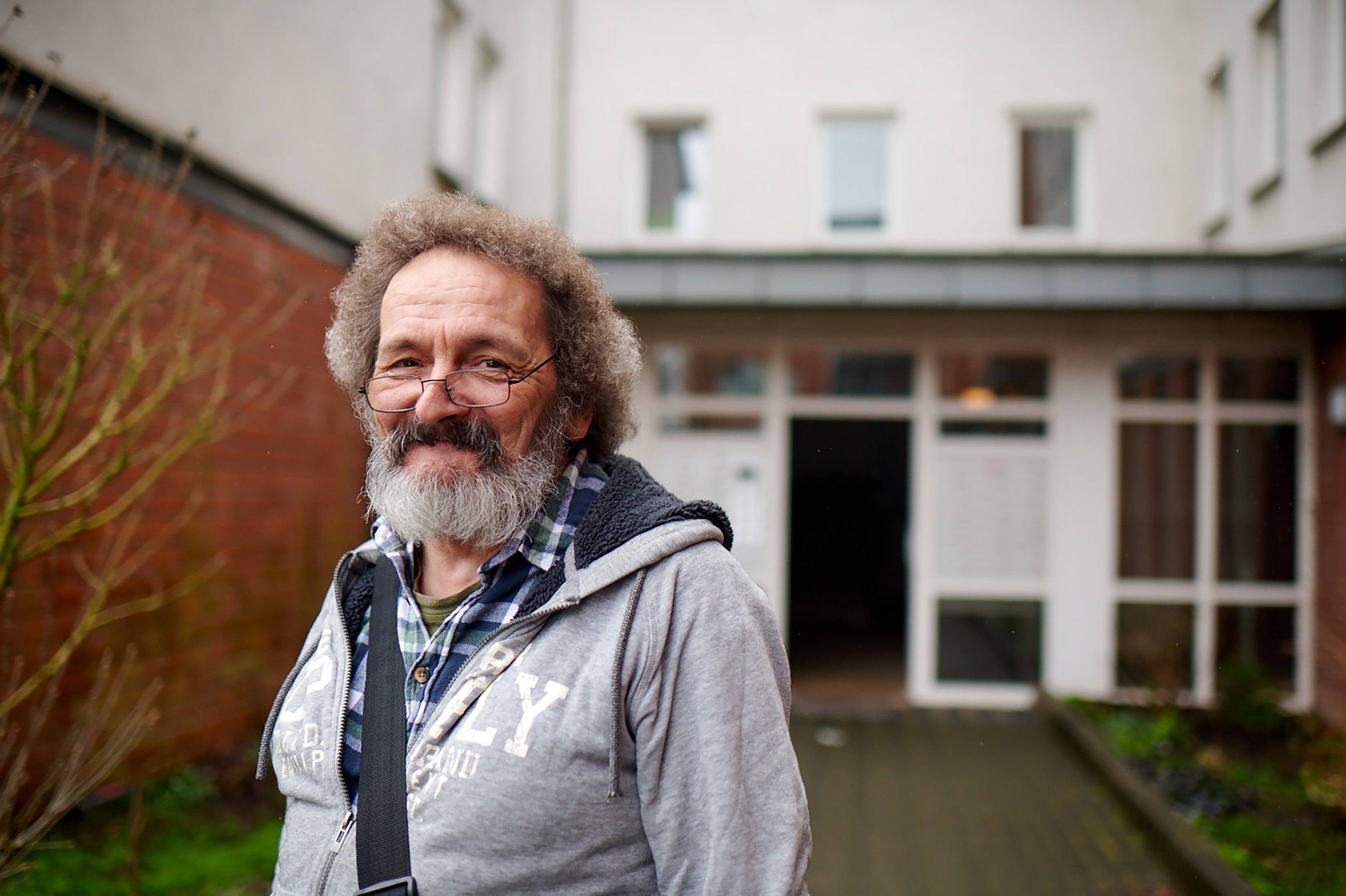 Mann mit Brille lächelt; steht vor Wohngebäude im Freien.