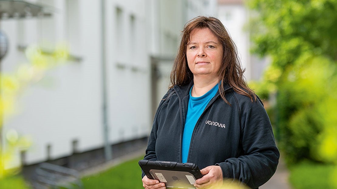 Frau hält Tablet, trägt Vonovia Jacke, steht draußen vor Gebäuden.