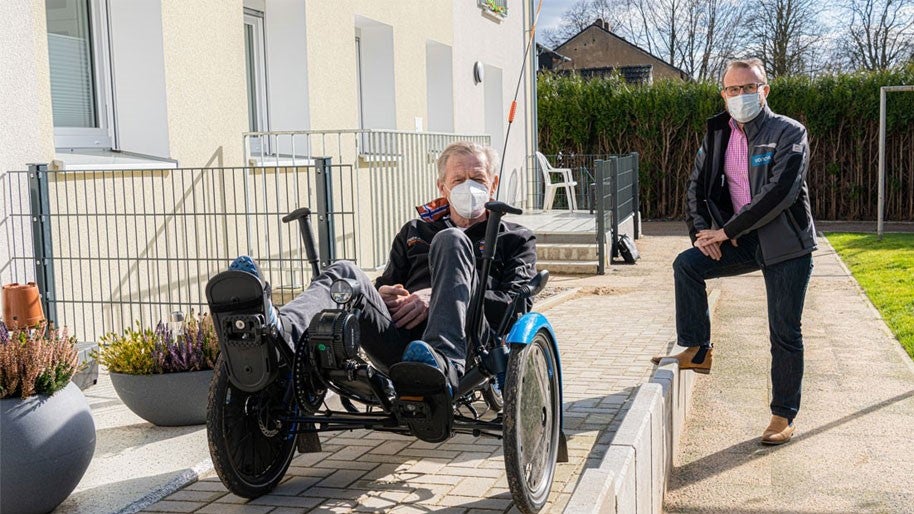 Mann fahrend auf Liegefahrrad vor barrierearmer Wohnung