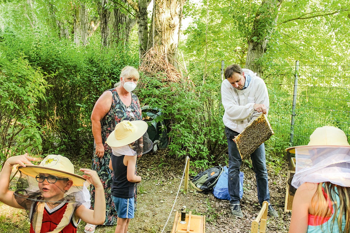 Kinder beobachten einen Imker im Wald beim Arbeiten mit Bienen.