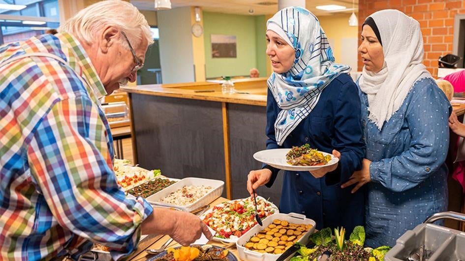 Mann, der an Buffet steht, und zwei kopftuchtragenden Frauen reden.
