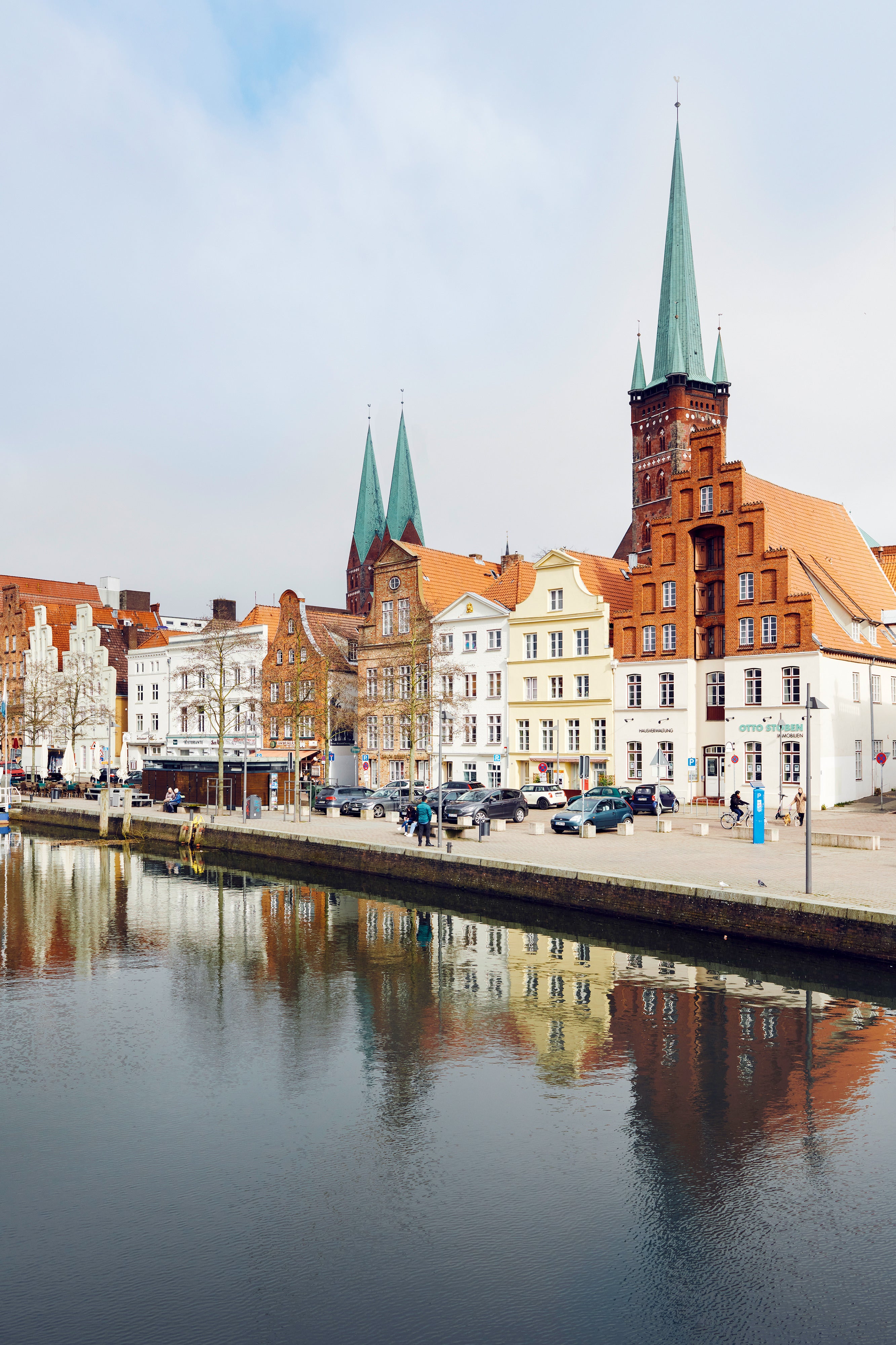 Kirchtürme spiegeln sich im Wasser vor alten Stadthäusern.