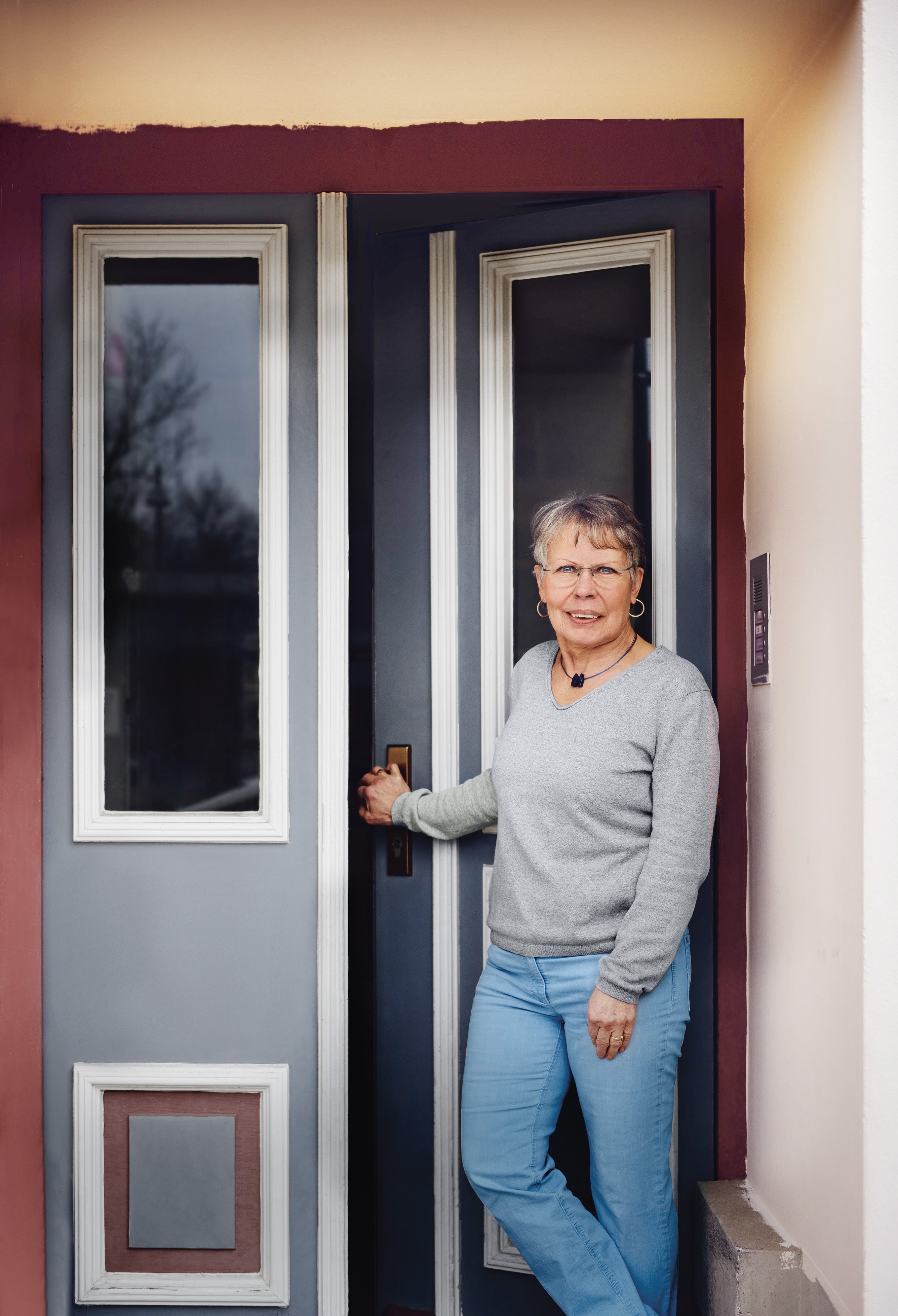 Frau öffnet die Haustür, stehend im Eingangsbereich.