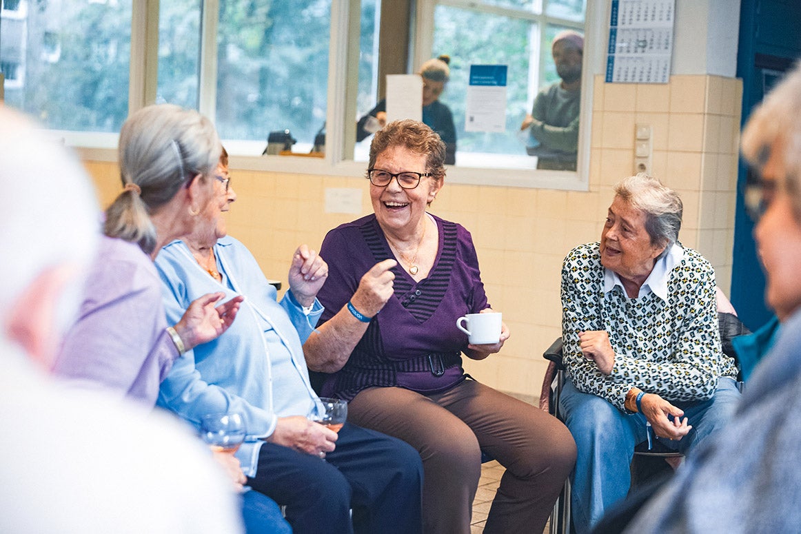Ältere Frauen sitzen, lachen und reden in einem Gemeinschaftsraum.
