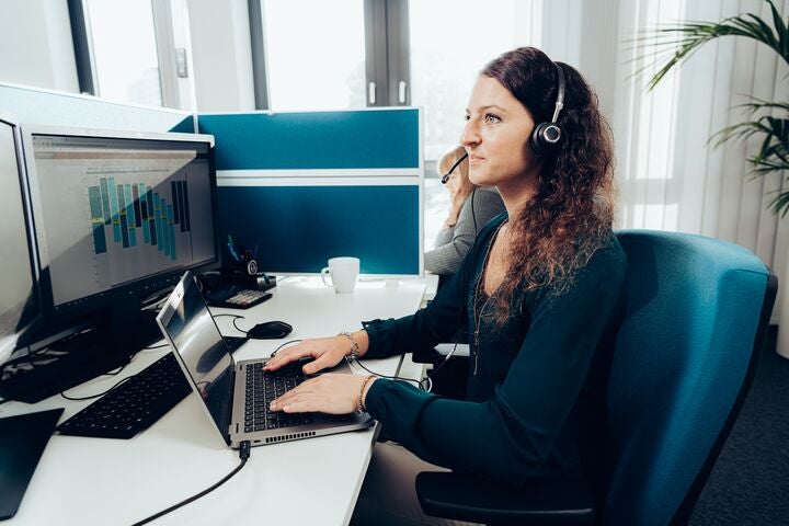 Frau arbeitet am Laptop im modernen Büro mit Headset.